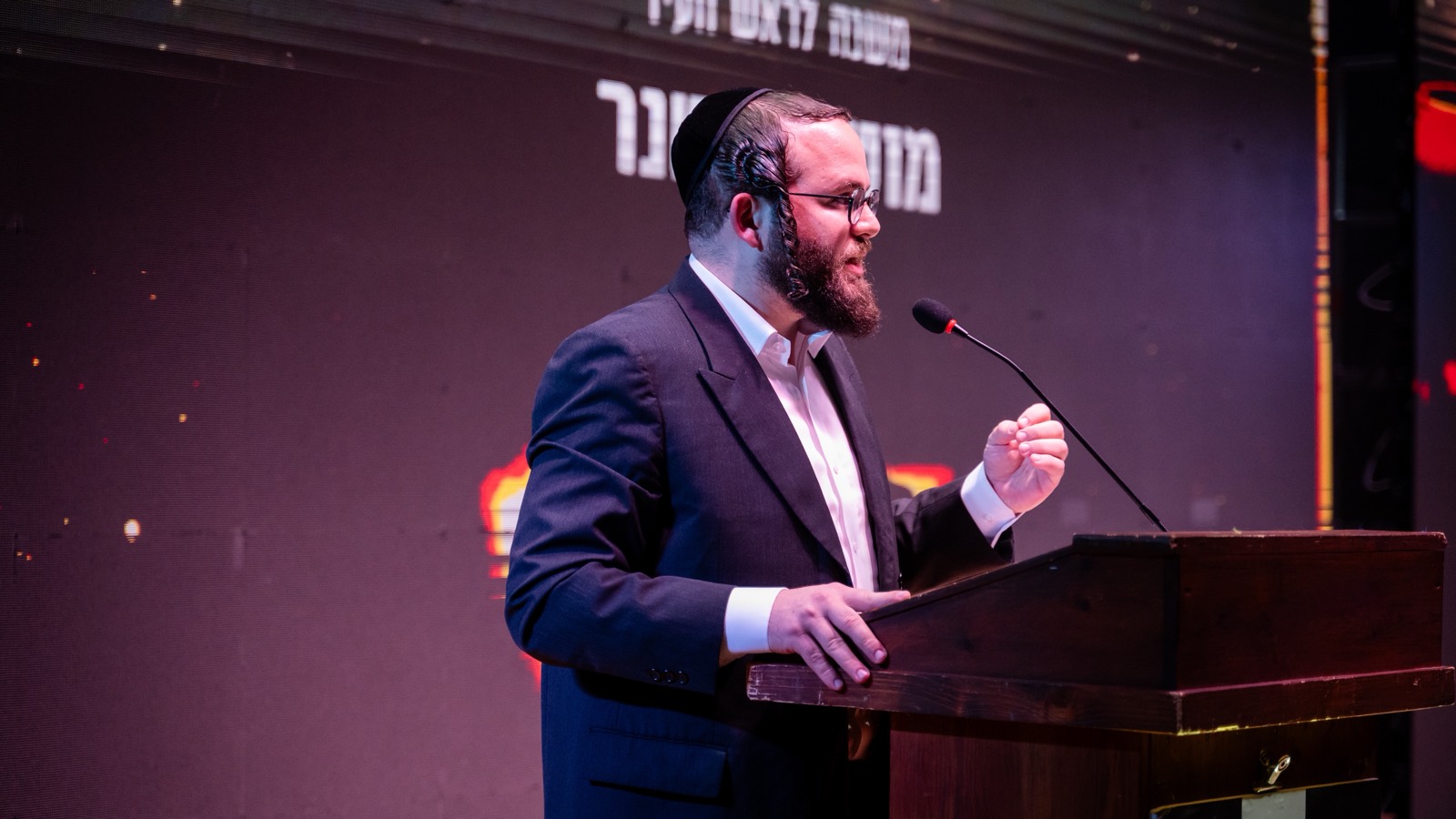 מוטי לייטנר נואם מאחורי דוכן על במה